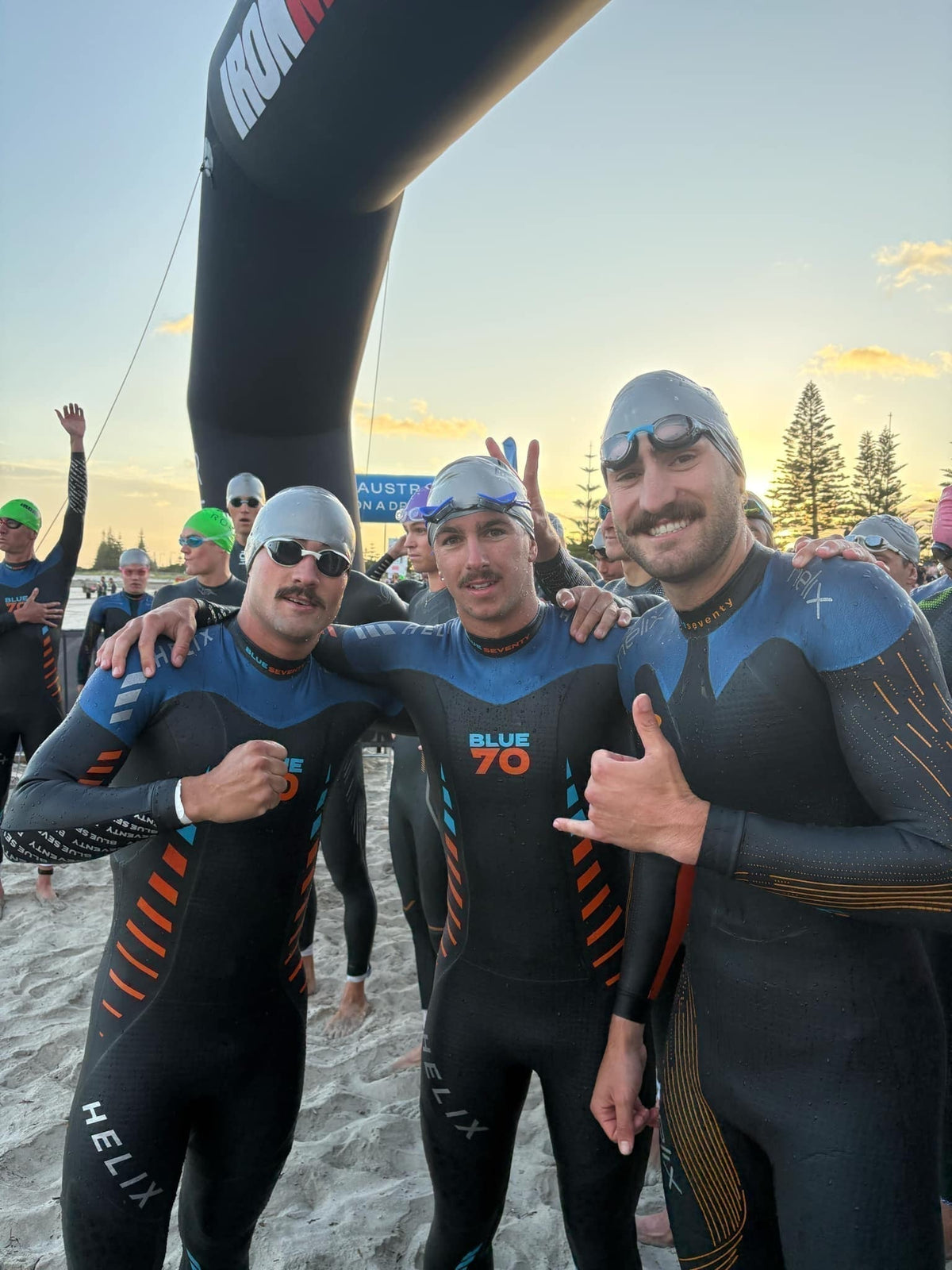 Busselton, December 2024. Ten minutes before the gun. Alt: Three triathletes in wetsuits arm in arm on the beach at sunrise before the start at Busselton.
