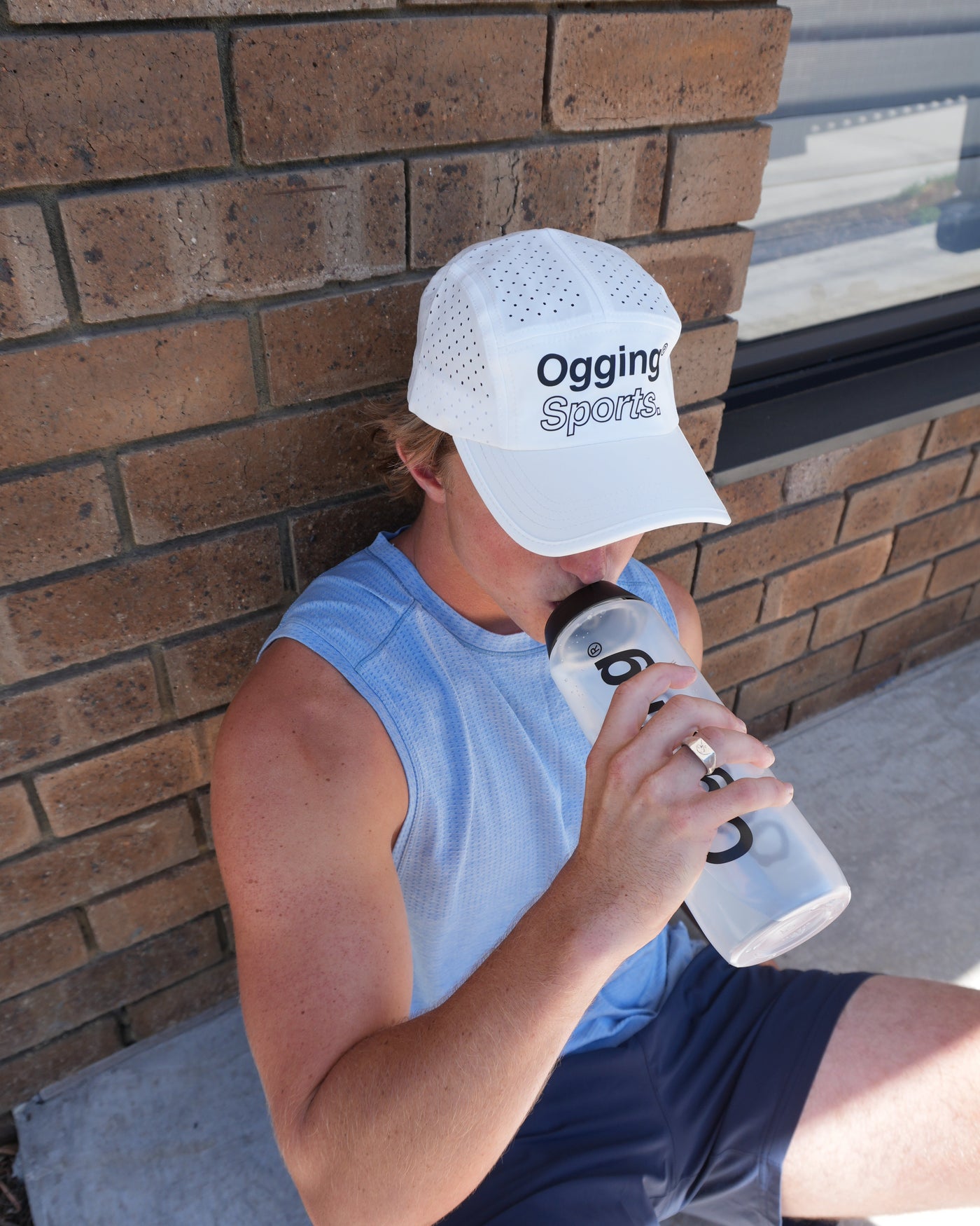 Person taking a break from exercise, leaning against a wall with a water bottle.