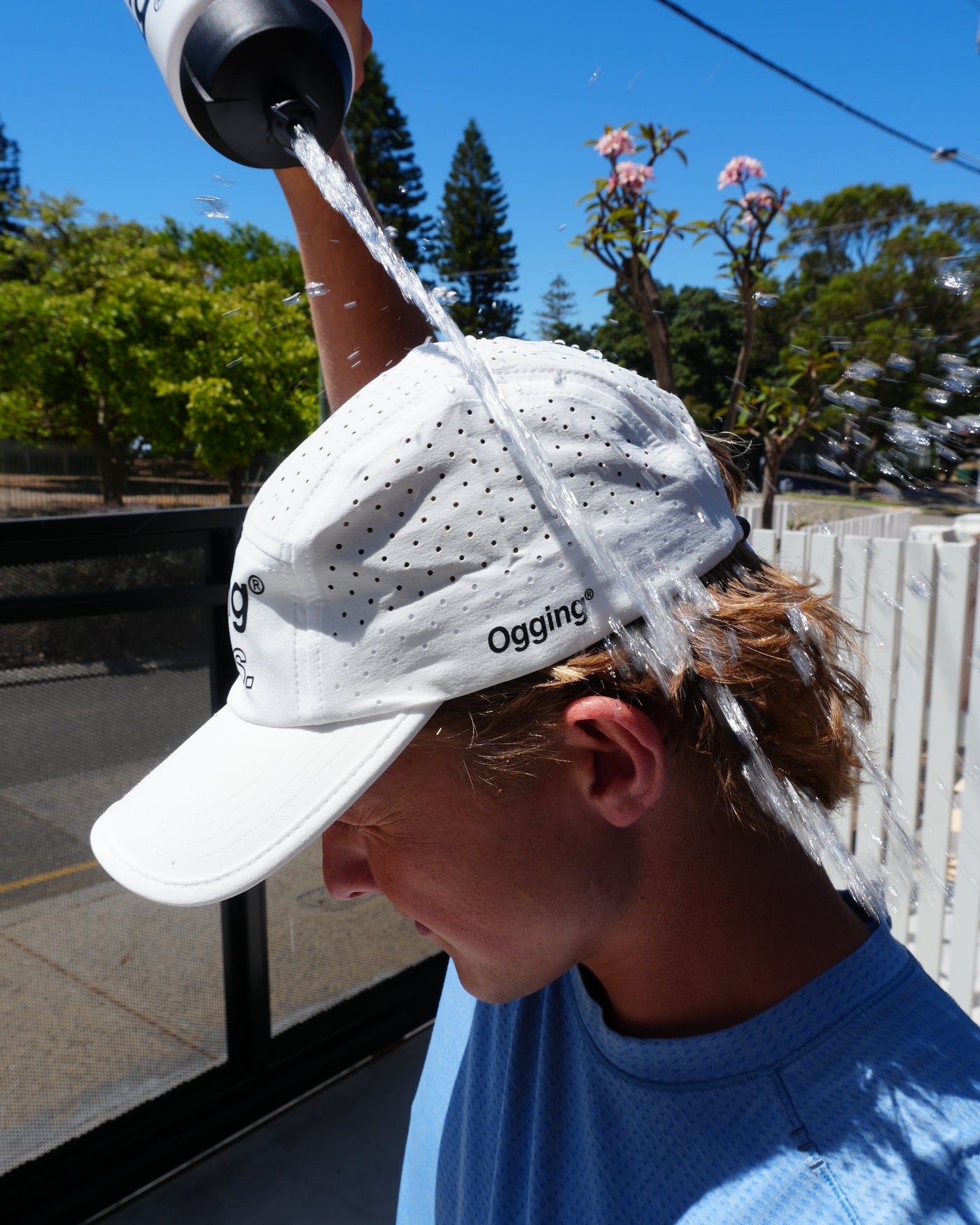 Person wearing a white cap with a logo, holding a water bottle outdoors.