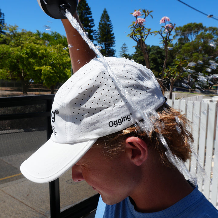 Person wearing a white cap with a logo, holding a water bottle outdoors.